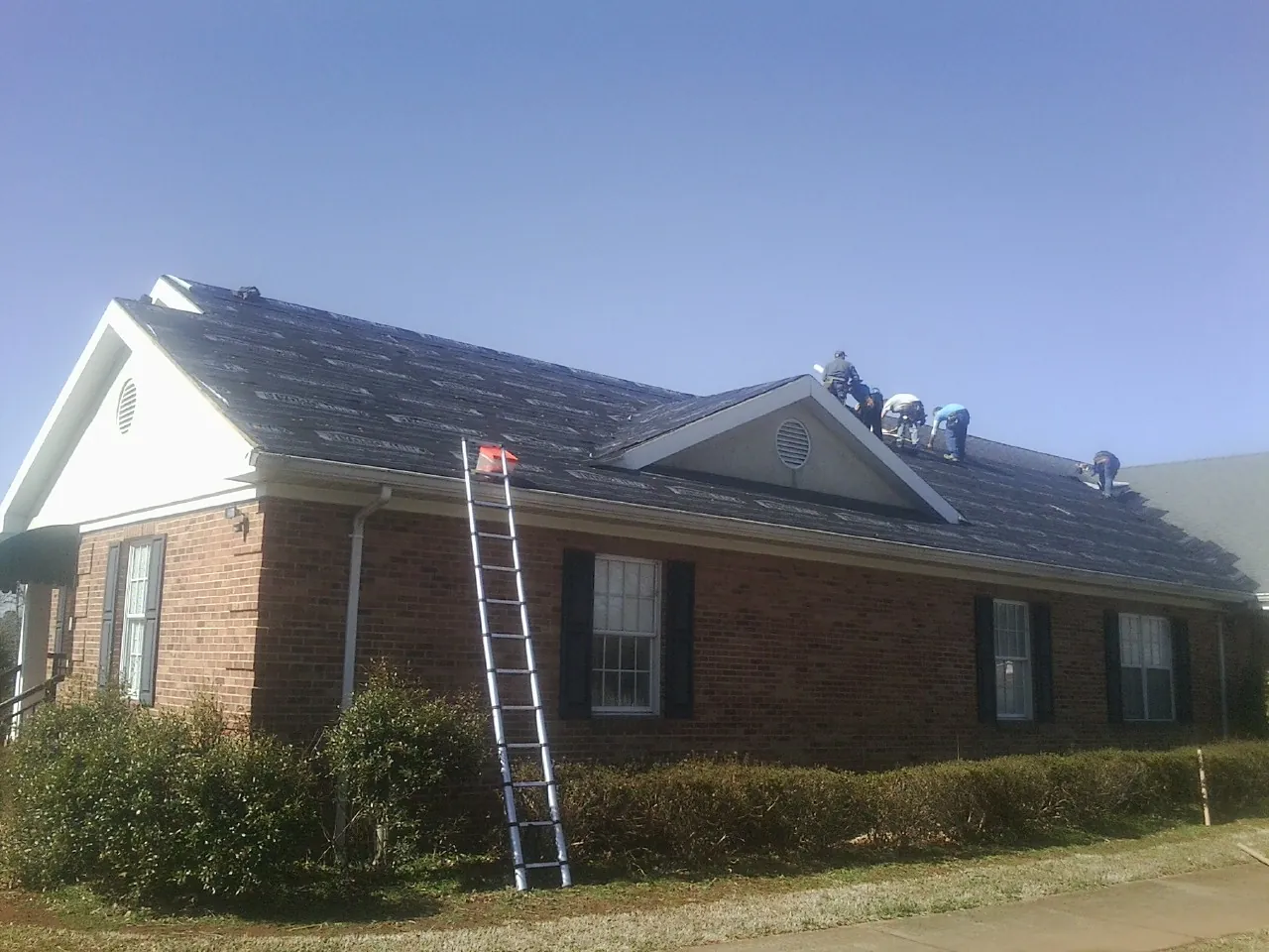 Crew tearing shingles off a brick ranch roof with a ladder set — Emergency Roof Repair work by our crew in Moundsville