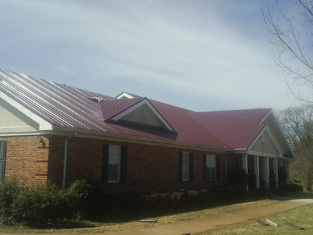 Red metal roof with gabled entries on a long brick building, from a Hail Damage Roof Repair job in Moundsville