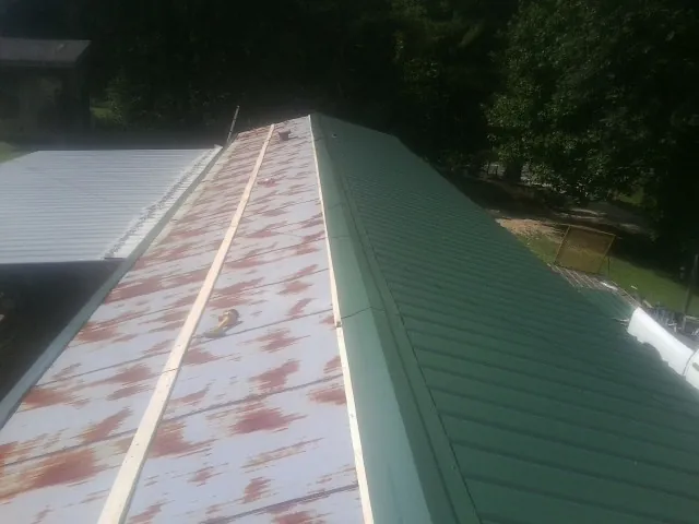 Old rusted panels beside newly installed green metal roofing — Wind Damage Roof Repair by Roofing Brothers in Moundsville