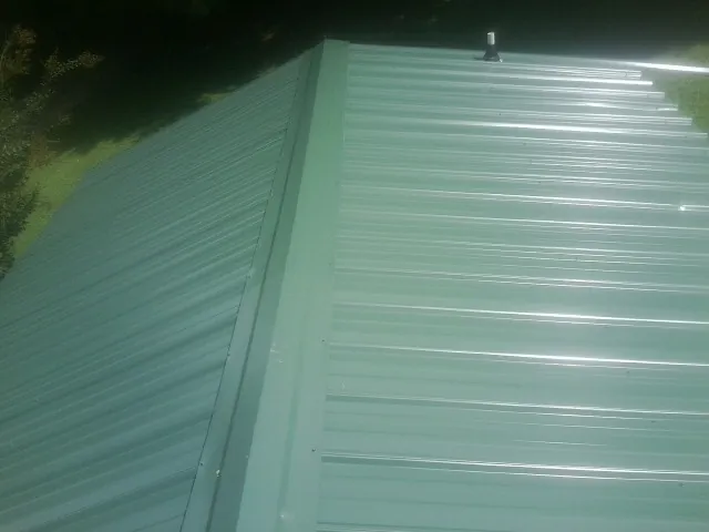 New green metal panels meeting at the ridge of a roof — Flat Roof Repair work by our crew in Moundsville
