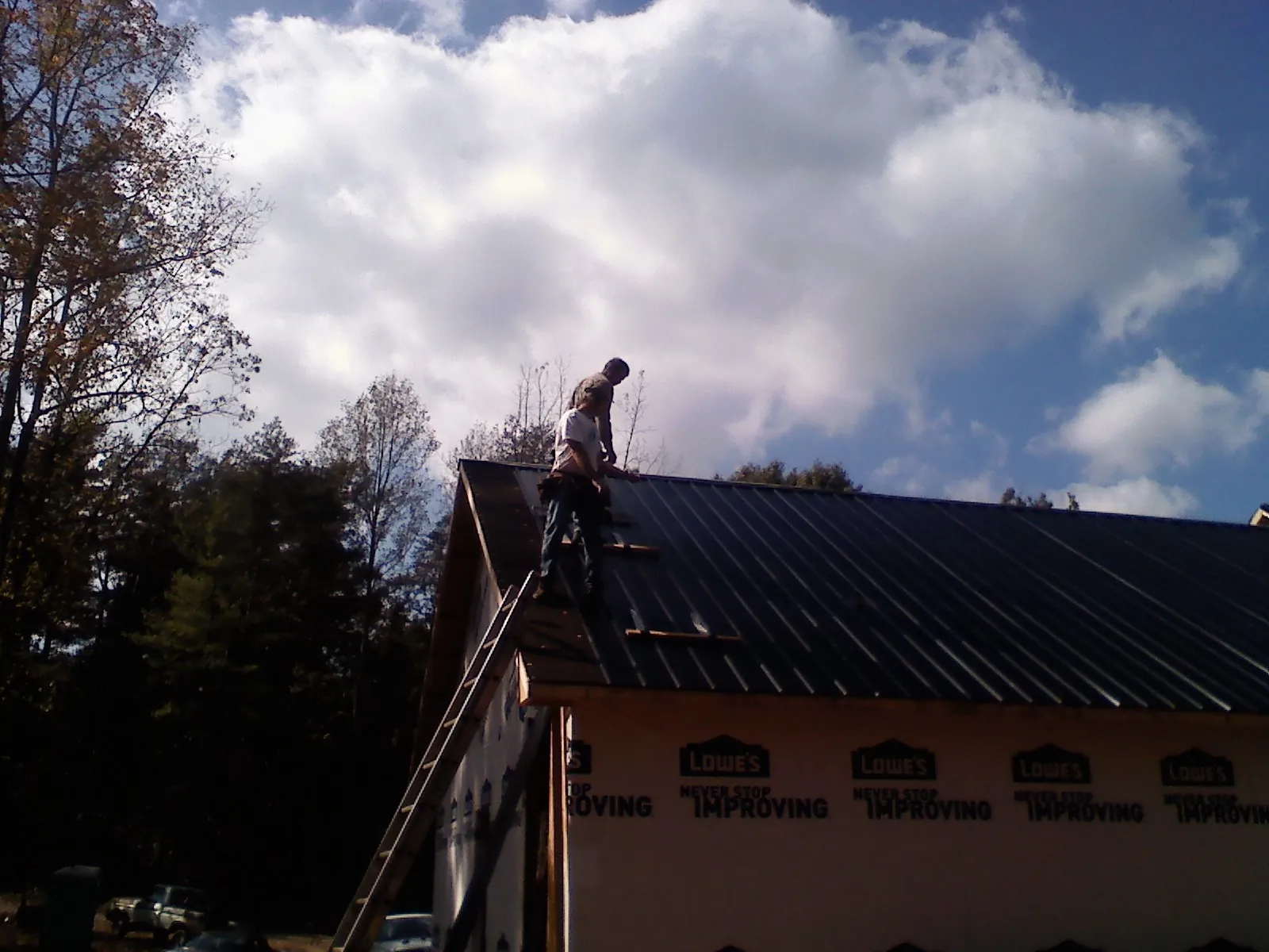 Roofer fastening dark metal panels high against a cloudy sky, from a Roof Inspection job in Moundsville