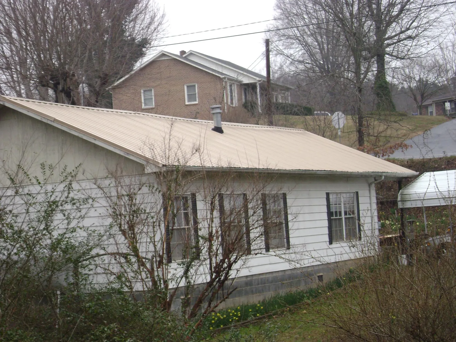 Tan metal roof on a white sided house set into a hillside — Commercial Roofing by Roofing Brothers in Moundsville